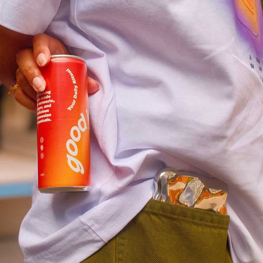 Oranje Good Jamu soda uit Starterpack in hand gestoken in broekzak. Gezonde frisdrank voor onderweg met authentieke Jamu smaken.